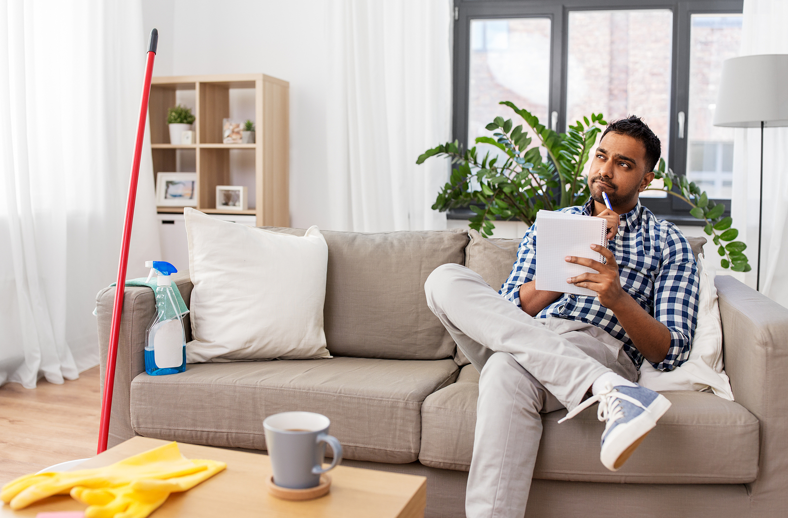 An indian man making to do list in notebook after home cleaning