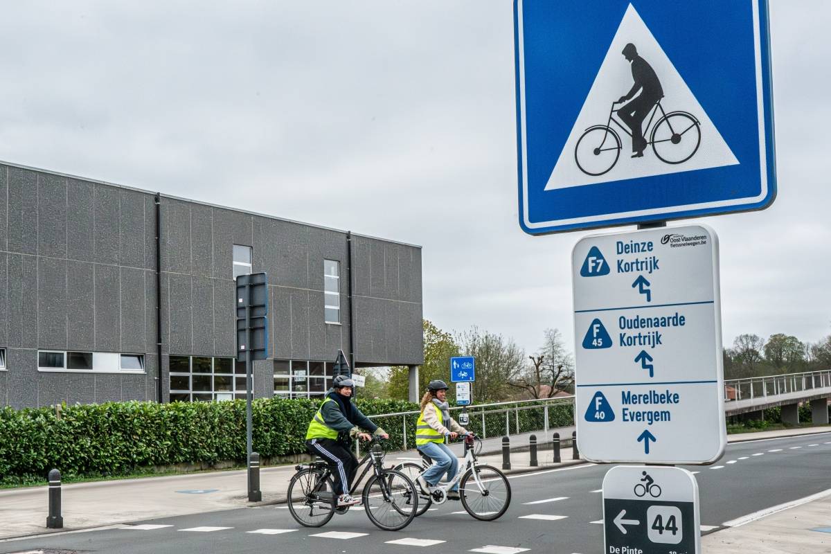 Panneaux de direction bleus des cyclostrades F7 et F4, avec deux cyclistes à l'arrière-plan