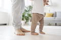 Baby practicing first steps barefoot with parent support