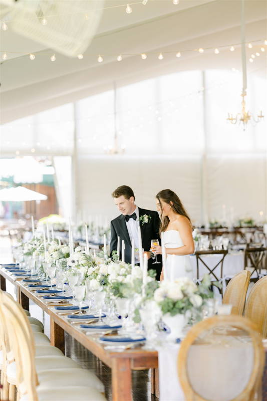 newlyweds looking over long farm table with white flowers