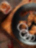 Spicy grilled chicken wings with onion rings on a black plate, garnished with chili flakes