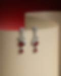 Stunning silver-toned drop earrings with red gemstones and diamond accents, displayed against a curved neutral backdrop with a red gradient.
