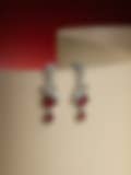 Stunning silver-toned drop earrings with red gemstones and diamond accents, displayed against a curved neutral backdrop with a red gradient.