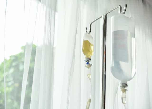 IV fluid bag with tubing and drip chamber attached to an IV stand near bright window curtains.