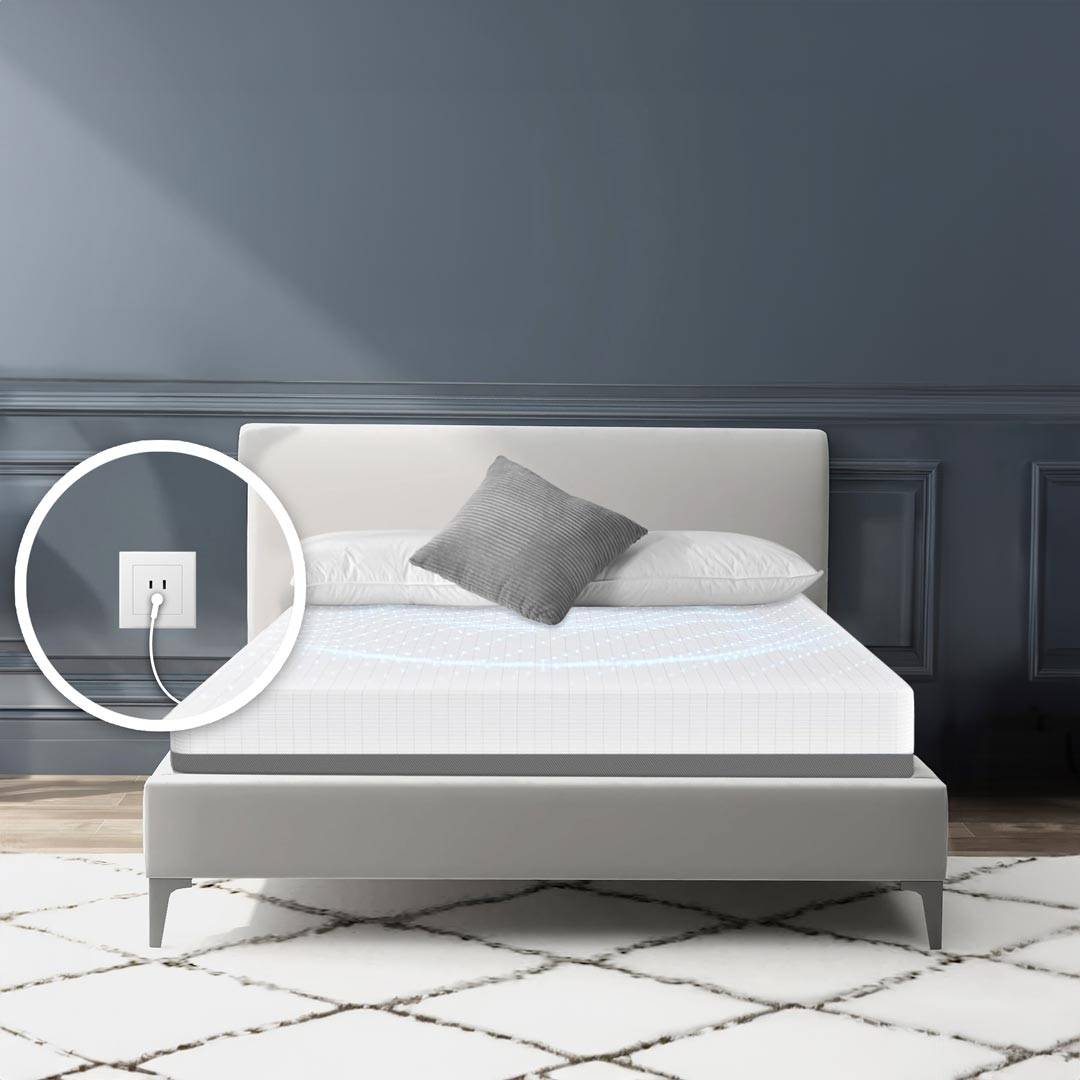 Bed with a gray pillow and a focus on a wall outlet with a plugged-in cord.
