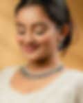 Smiling woman in a white traditional outfit wearing an elegant diamond and blue gemstone necklace with matching earrings, set against a warm golden background.