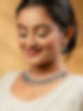 Smiling woman in a white traditional outfit wearing an elegant diamond and blue gemstone necklace with matching earrings, set against a warm golden background.