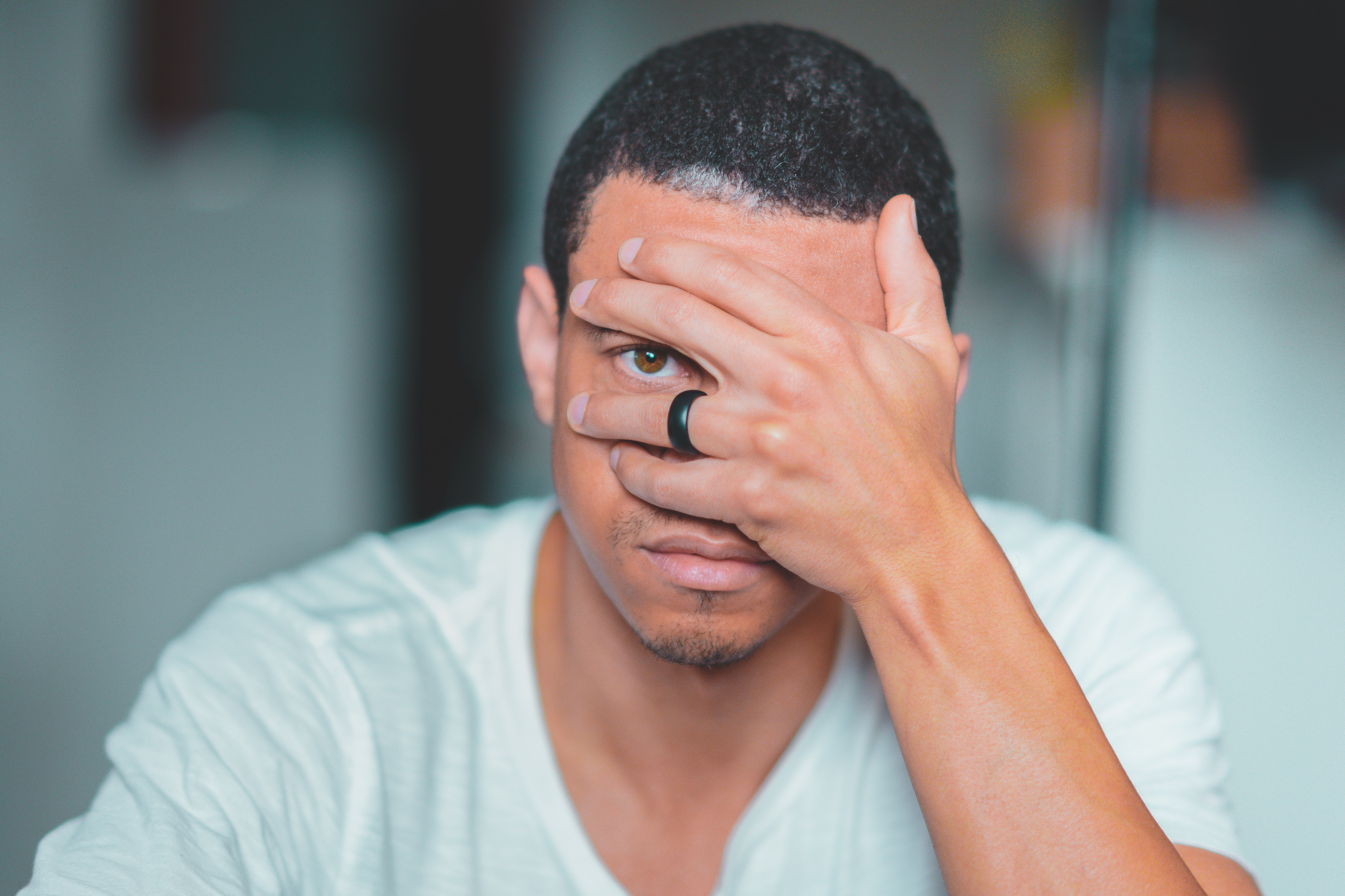 A multiracial man with short hair, covering his face except for one eye that he looks through.