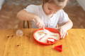 Toddler enjoying sensory play using a spoon to scoop sugar in a red plate.