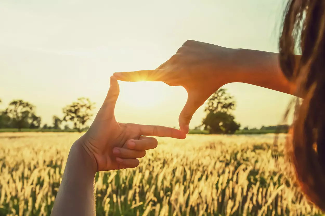 Phoot of a person putting their thumb and index fingers from both hands into a square shape and holding it up to the sky as the sunrises, like they're looking through a window.