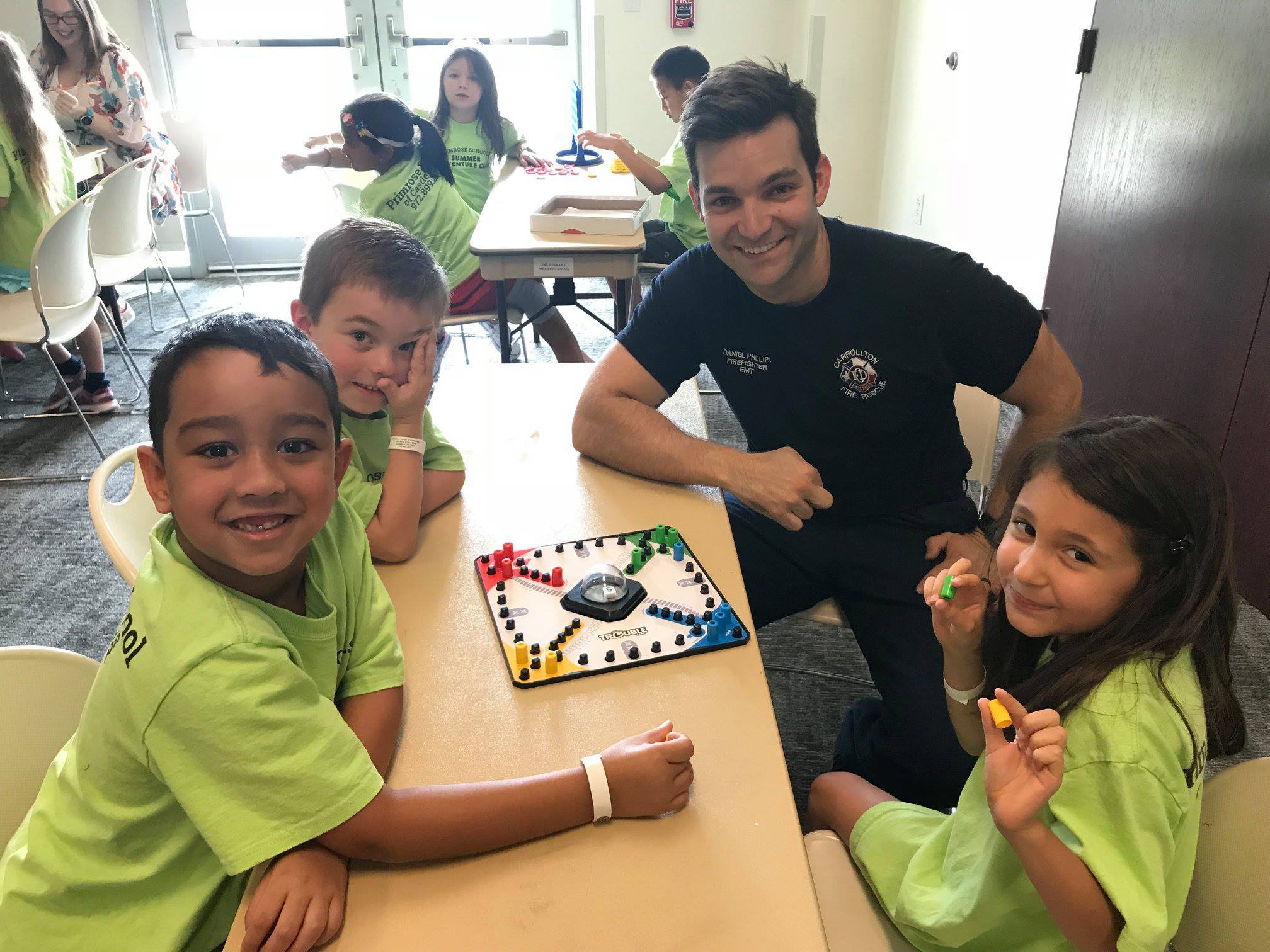 Image of three children playing a board game with a firefighter around a table. 