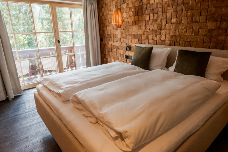 Natur Schlafzimmer mit Doppelbett, Holzpaneelwand und Fenster mit Balkonblick im Apartment von Hugo & Pepi in Mittelberg im Kleinwalsertal.