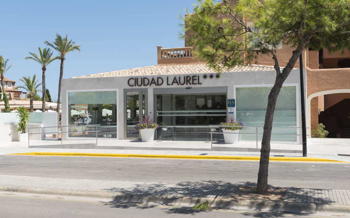 Der Eingang des Hotels Ciudad Laurel mit weißer Fassade, Glastüren und barrierefreiem Zugang.