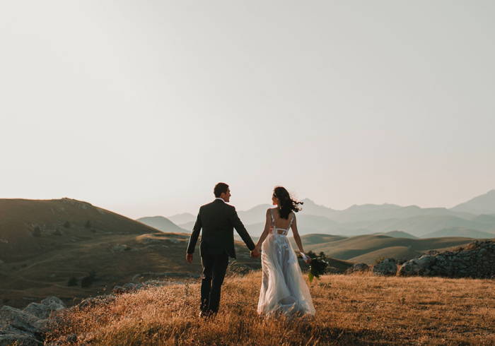 Photo de mariage d'un homme et une femme élégamment vêtus marchant main dans la main en pleine nature