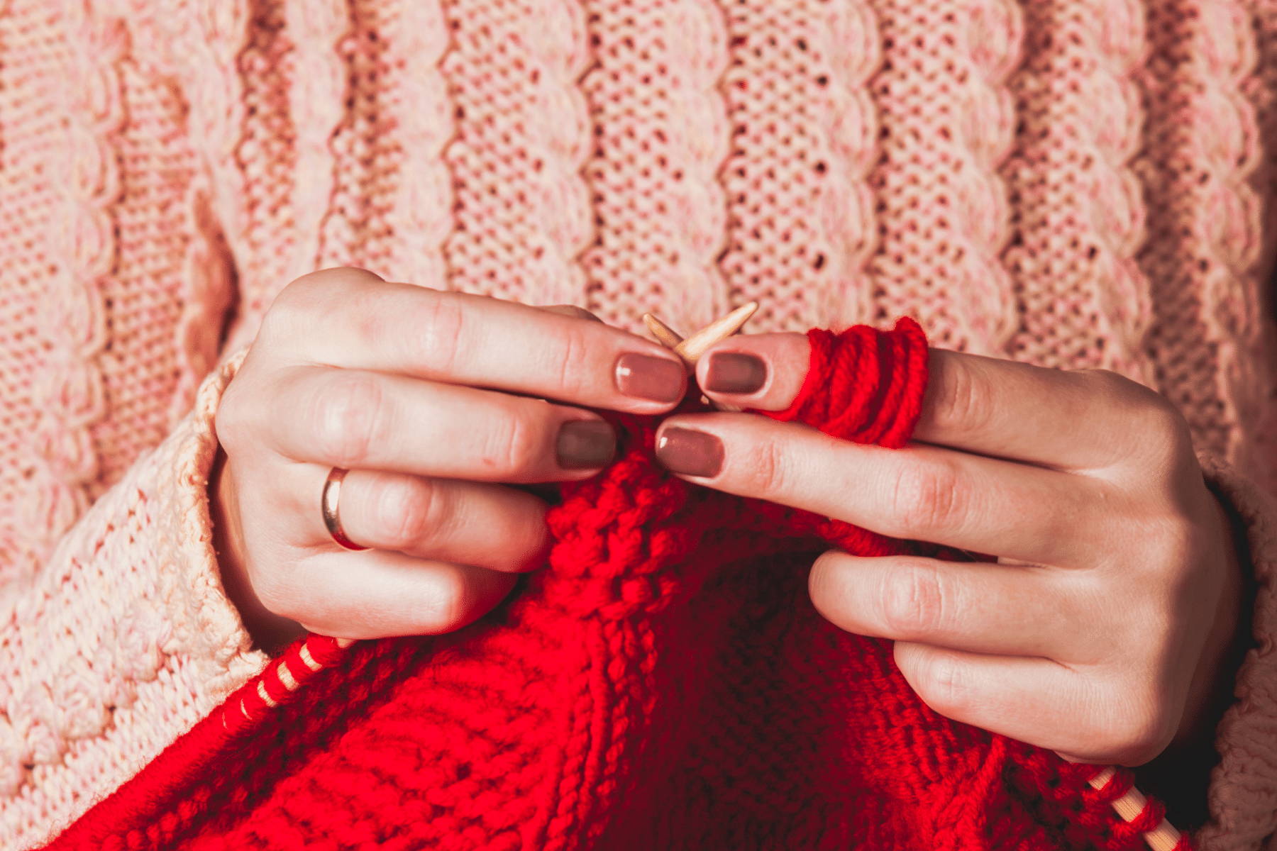 Woman in pink sweater knitting a red sweater