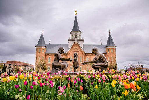 Provo City Center picture featuring a bed of tulips and a statue of young parents helping their little child walk.