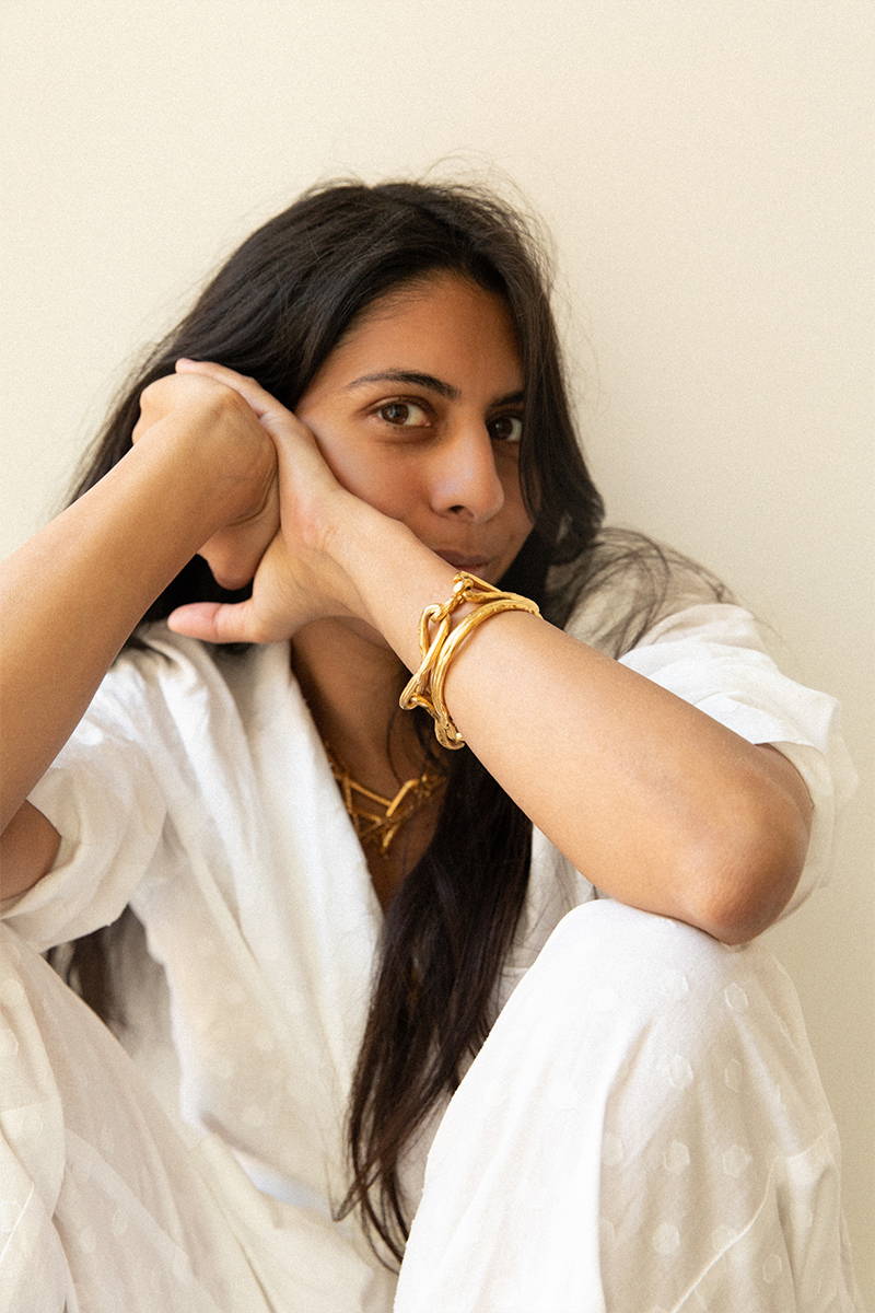 Rosh Mahtani smiles at the camera in YOLKE's Jacquard White Cotton Classic Pyjamas and Alighieri Jewellery 