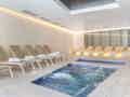 Moderner Indoor-Spa-Bereich mit einem sprudelnden Whirlpool, kleinem Becken und beigefarbenen Liegestühlen bei sanfter Beleuchtung.