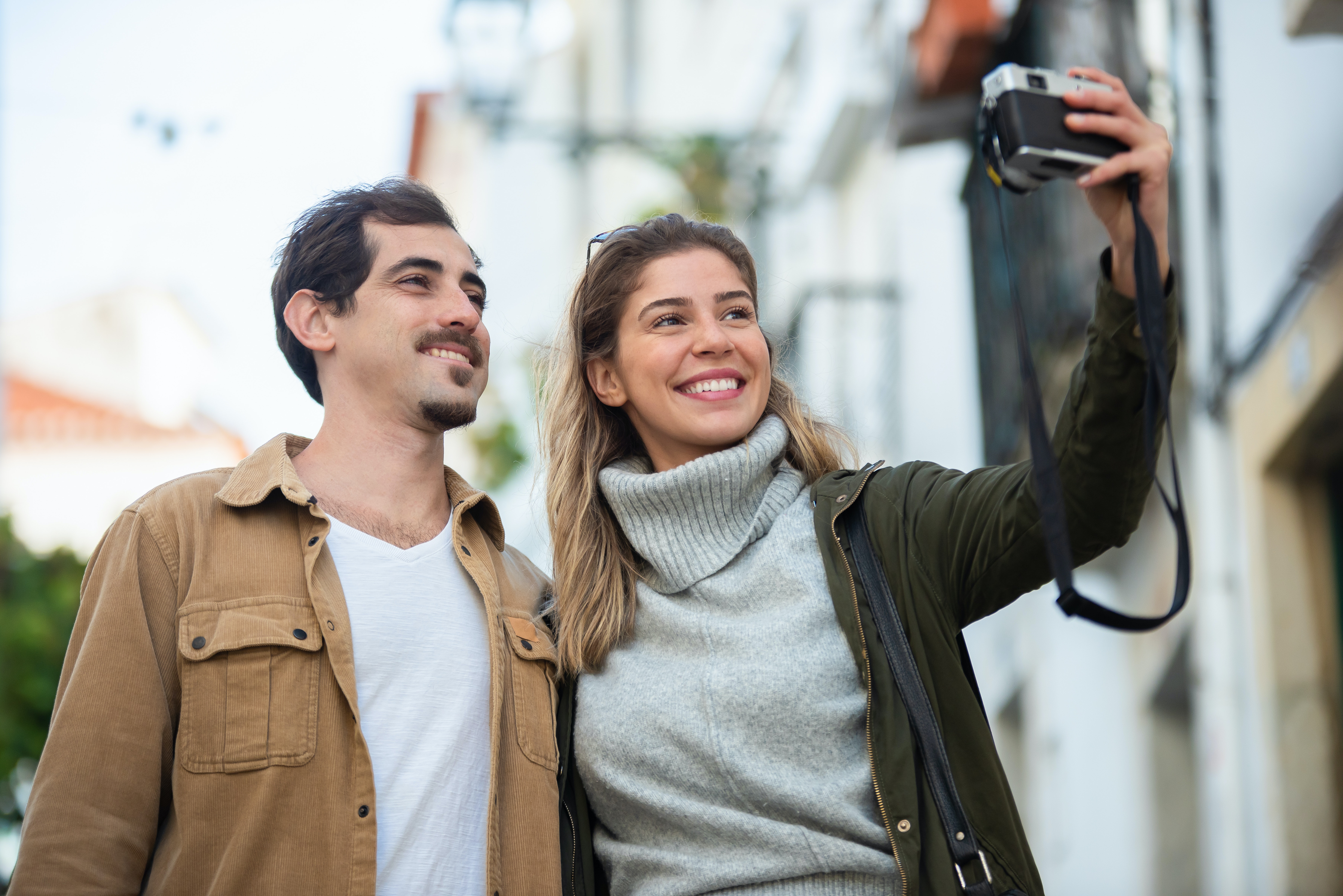 A man and a woman stand close to eachother while she holds outa camera to take a picture of both of them while they smile.
