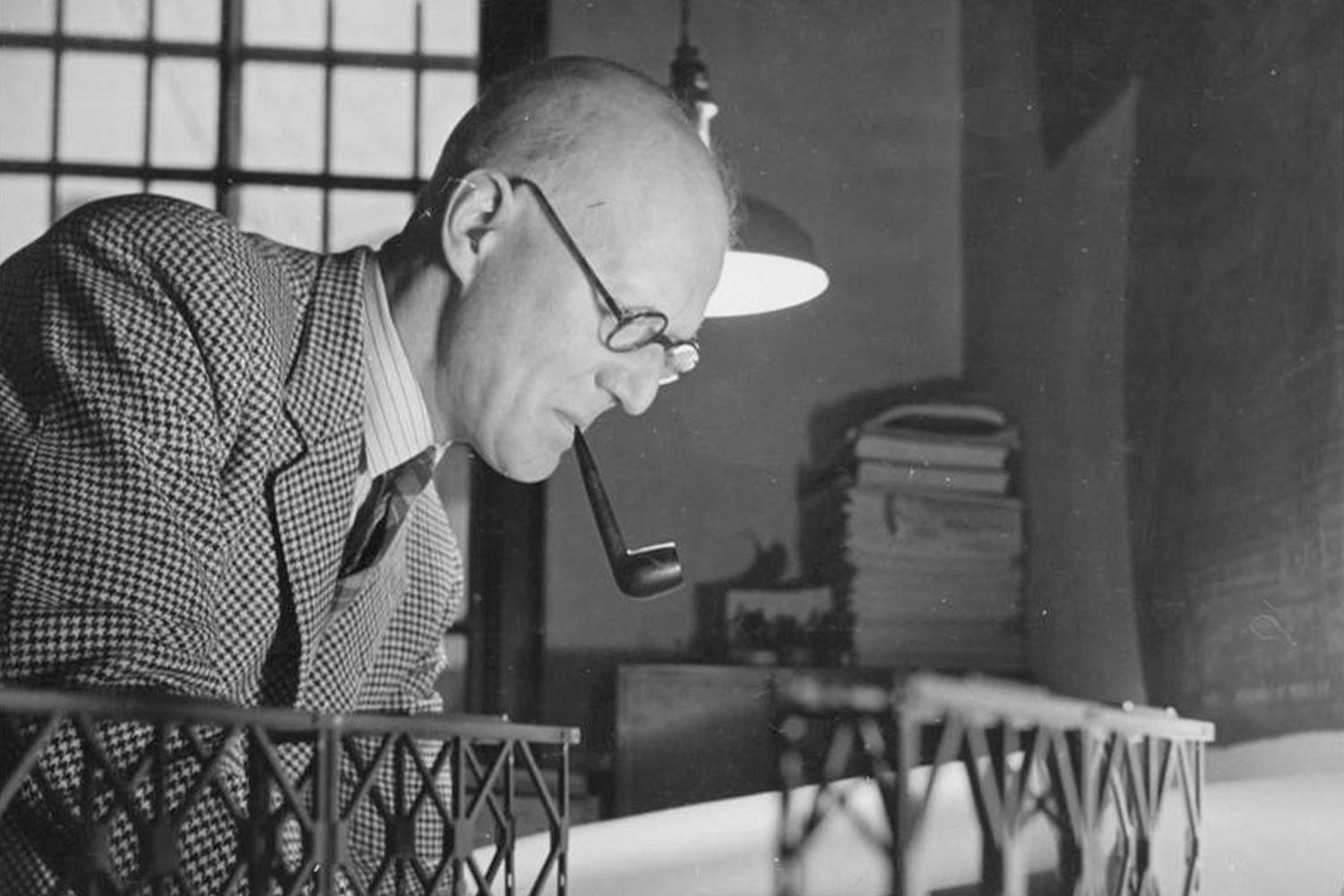 A black and white picture of a man in a suit working at his desk while smoking a pipe