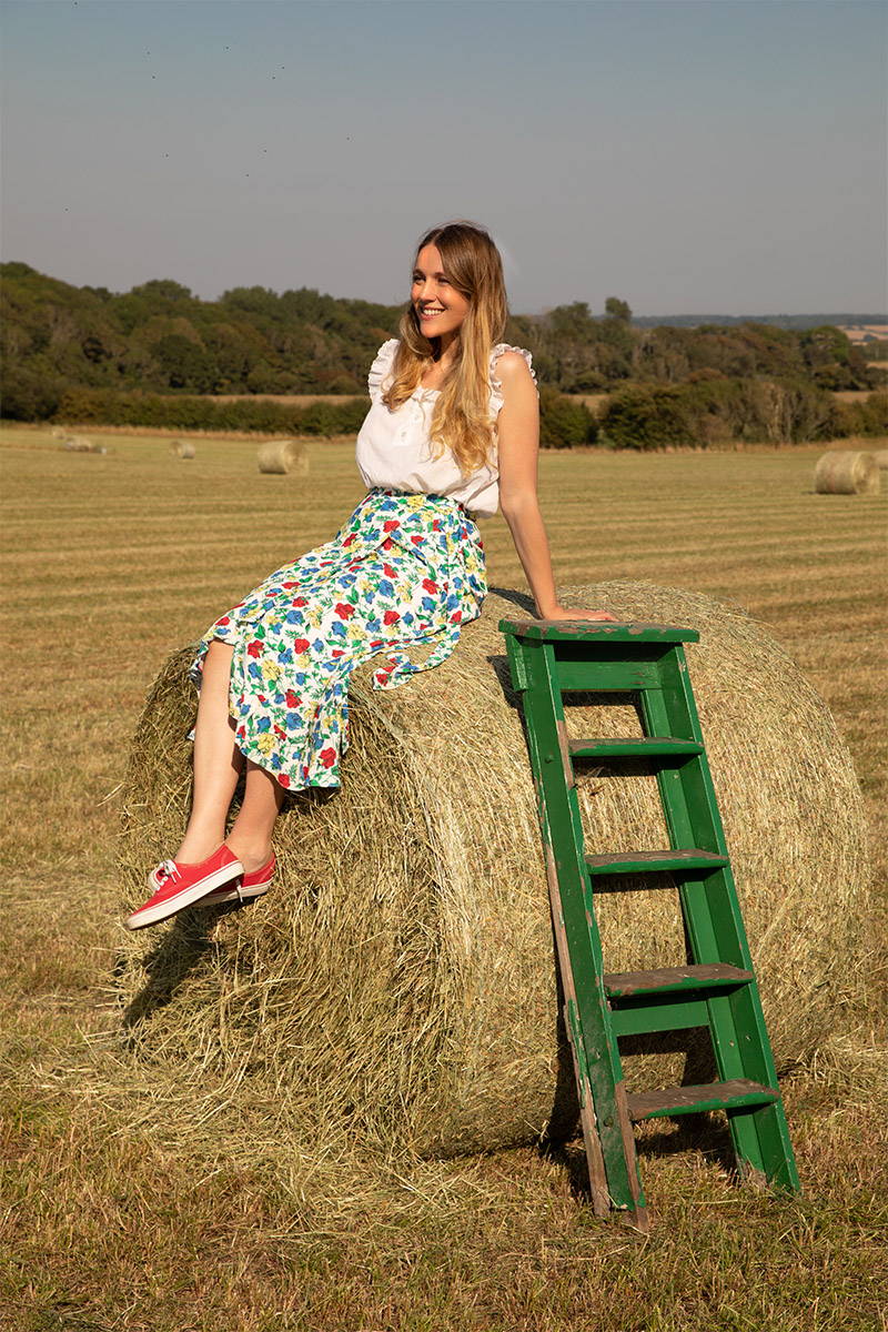 Tess Newall perches on a hay bale whilst wearing YOLKE