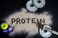 protein spelled out in whey protein powder next to weights