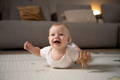 Smiling baby practicing tummy time on a soft play mat while holding a small wooden toy