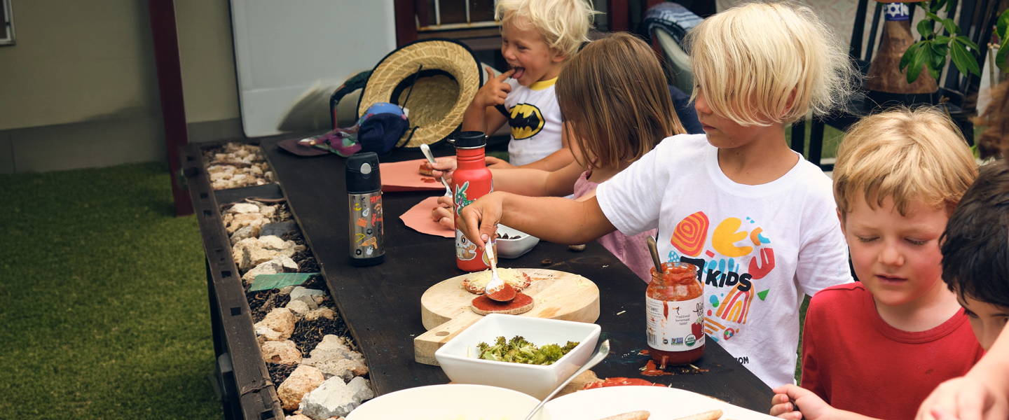 Group of children enjoying PACHA sprouted buckwheat bread and English muffins together at a long table.