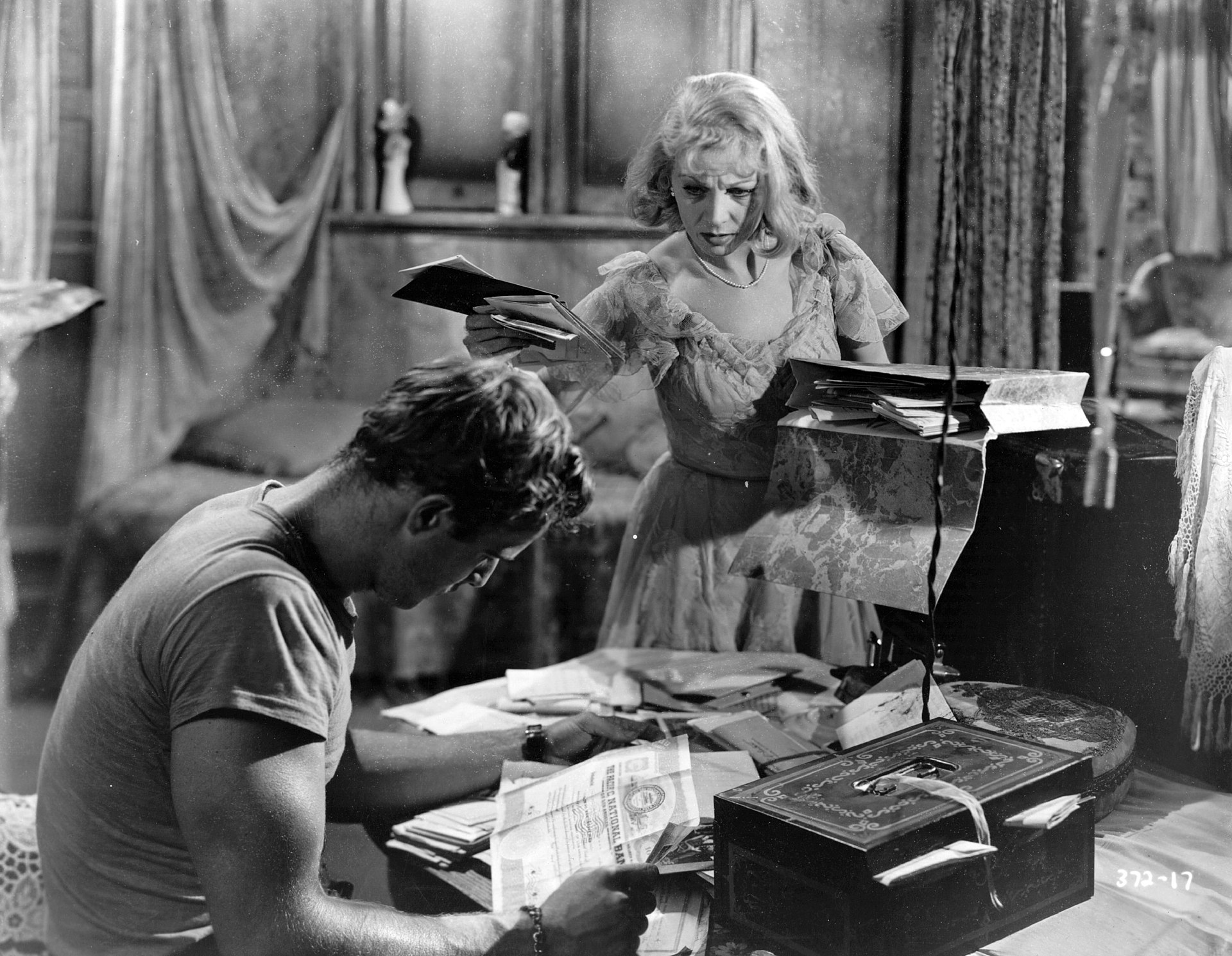 Marlon Brando sits on a desk reading a book while Vivien is talking to him holding a book in her hand.