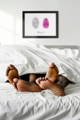 black couple's feet at end of bed with fingerprint artwork hung above headboard