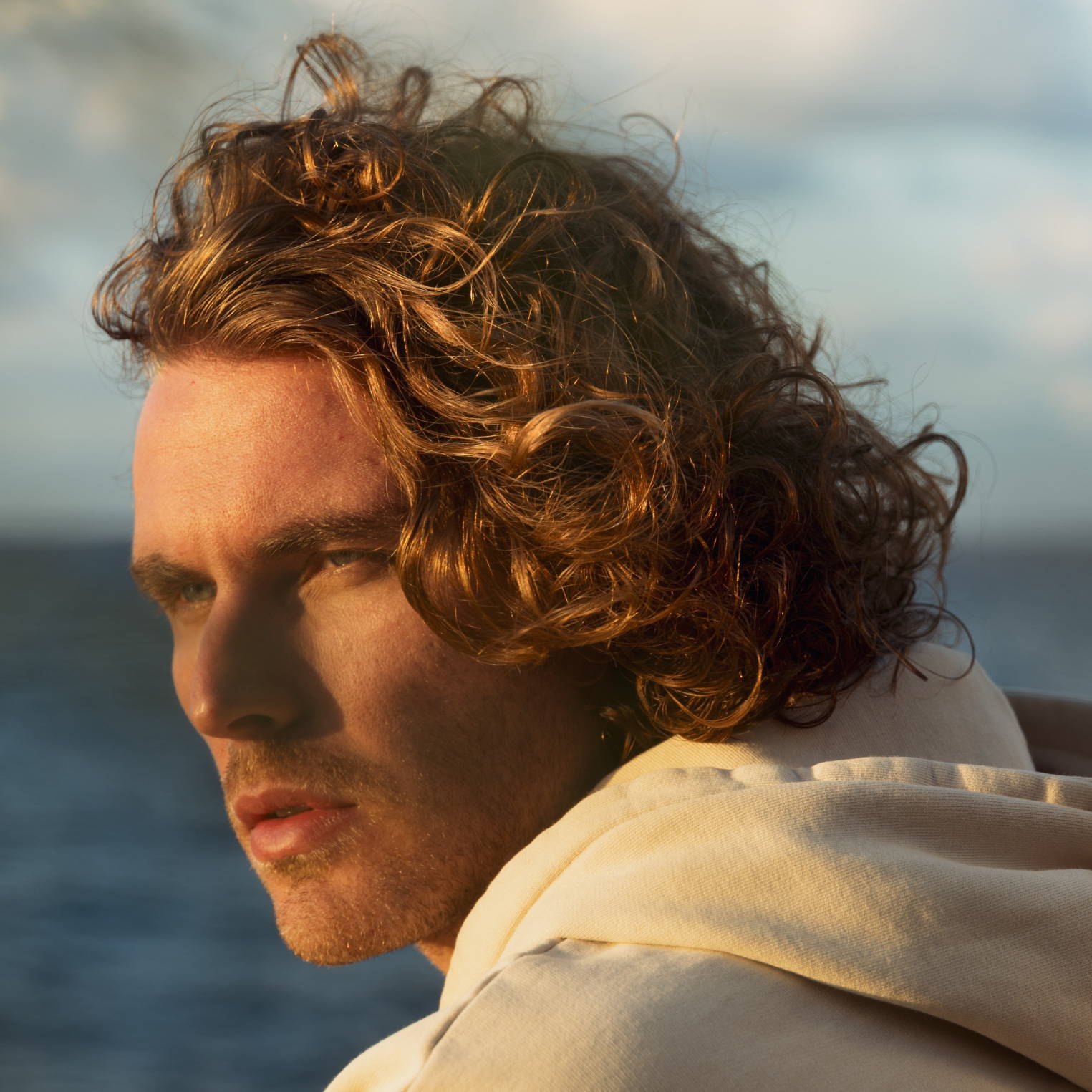 Man with golden, curly hair sitting by the ocean