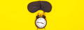 A visual represenation of  sleep, a black sleeping eye patch and old fashioned alarm clock on a yellow background