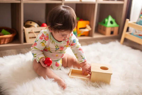 Little girl playing with the Montessori Object Permanence Box and taking a red ball out of the wooden box.