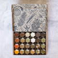 A decorative cardboard box contains 24 glass spice jars filled with various spices