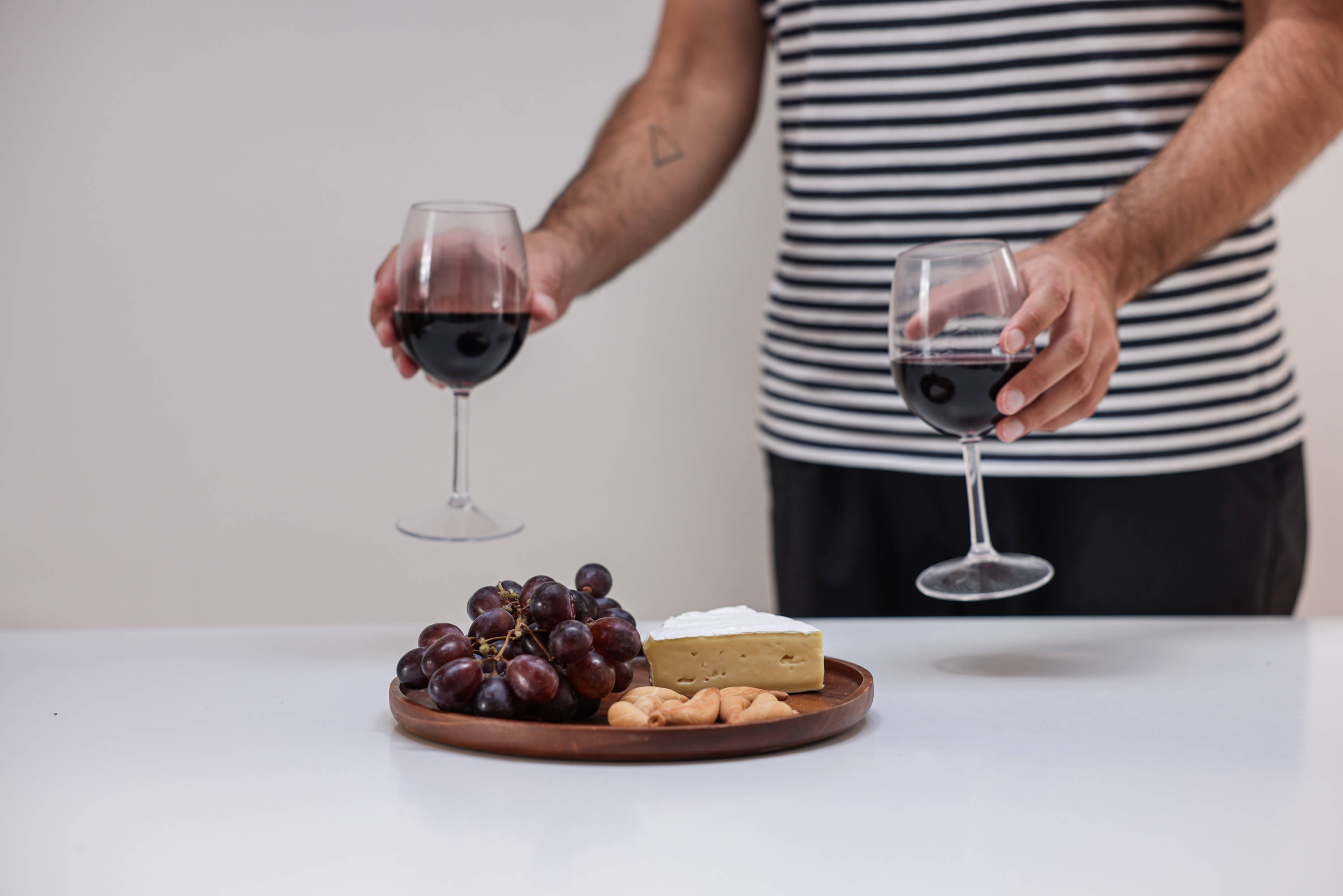 Two glasses of red wine alongside a plate of nuts, cheese and red grapes. 