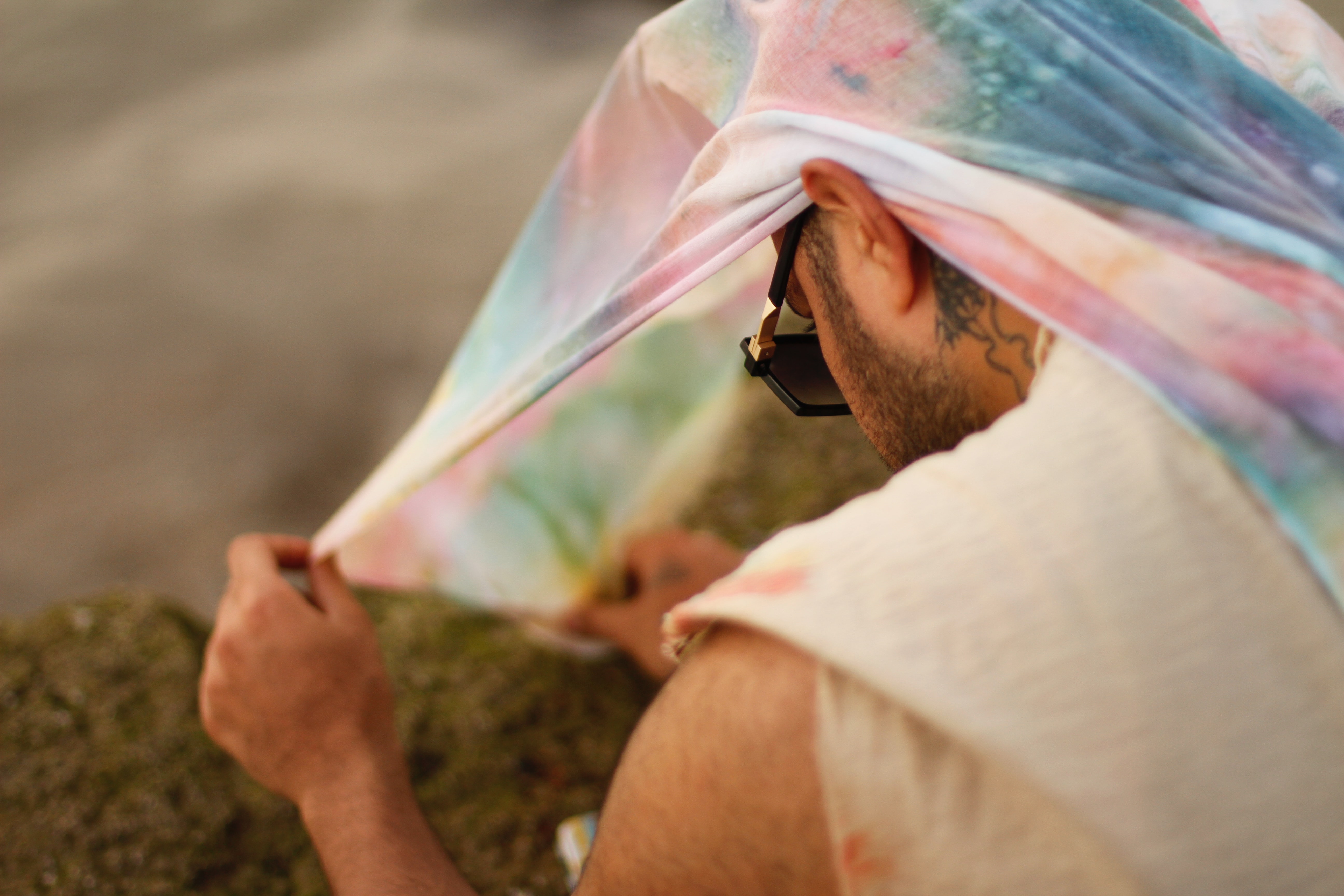 A man is crouching looking at his tie dye cloth over his head.