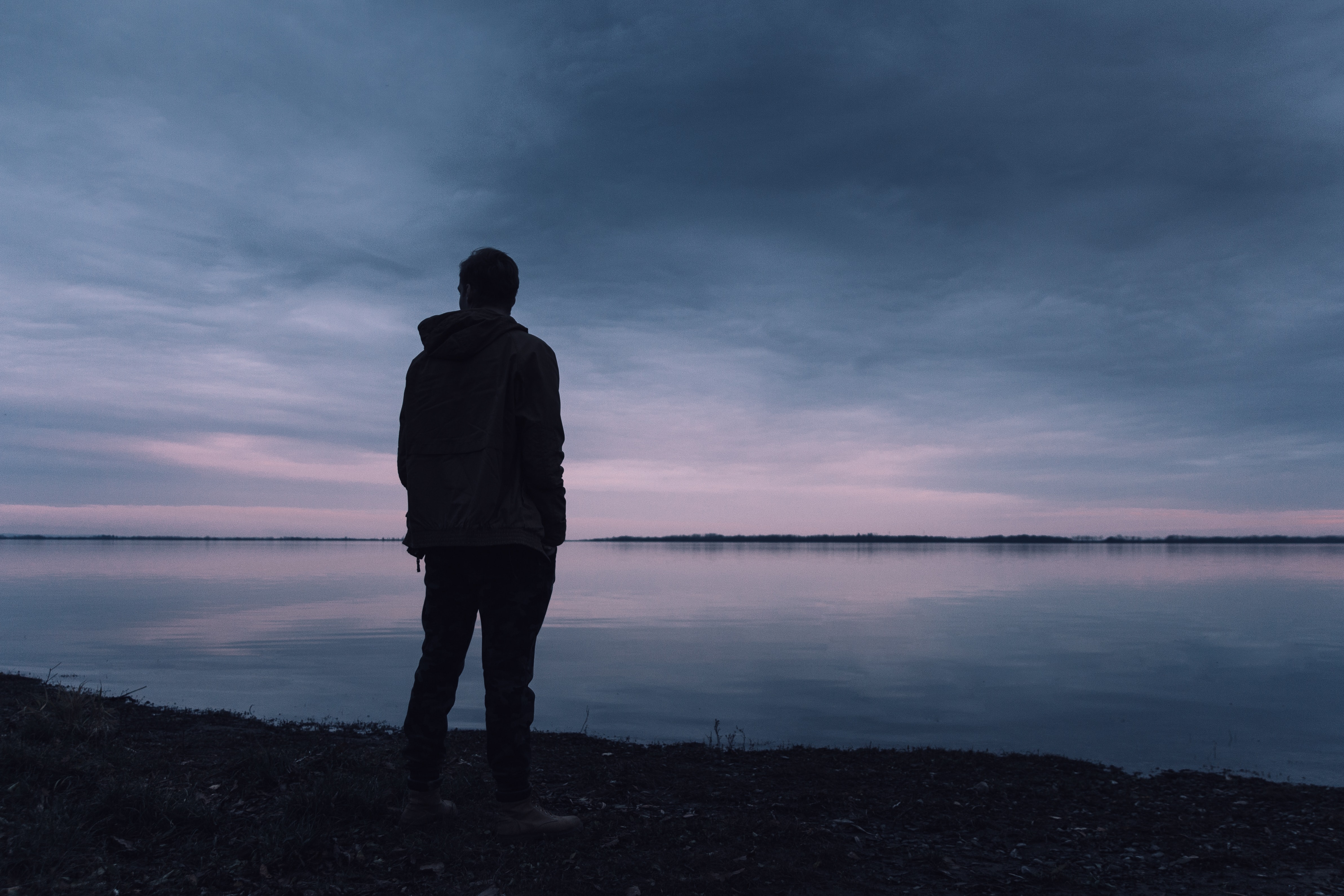 The silhouette of a man overlooking a lake in the early morning while it is still dark.