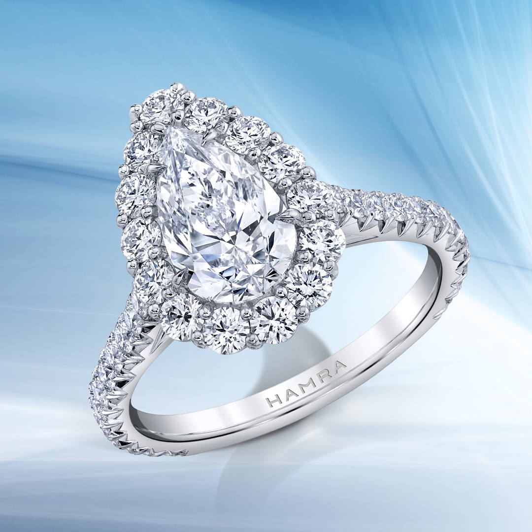 Pear shaped diamond ring with diamond halo in white gold on a blue background.