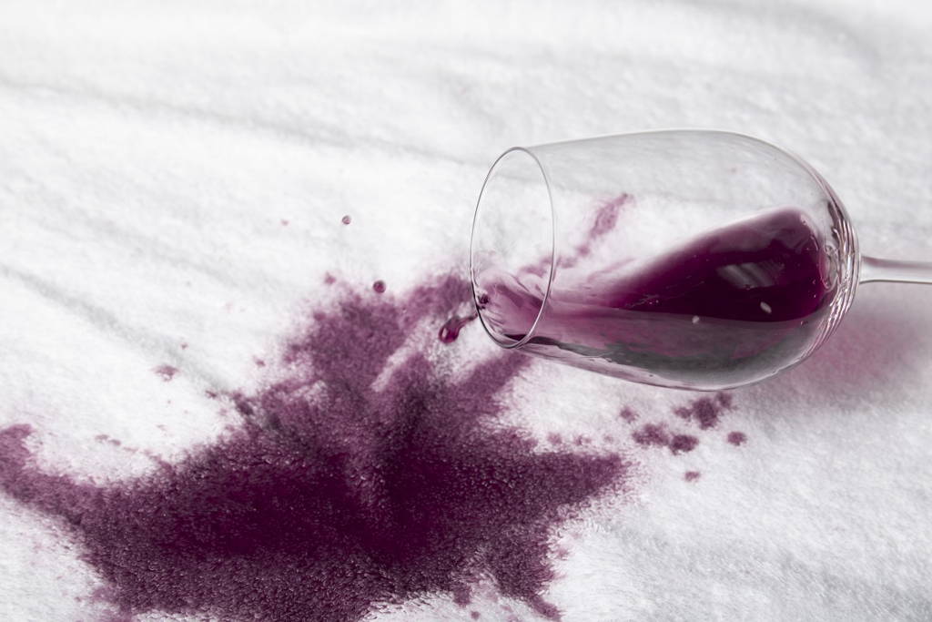 Glass of red wine spilling on white table cloth.