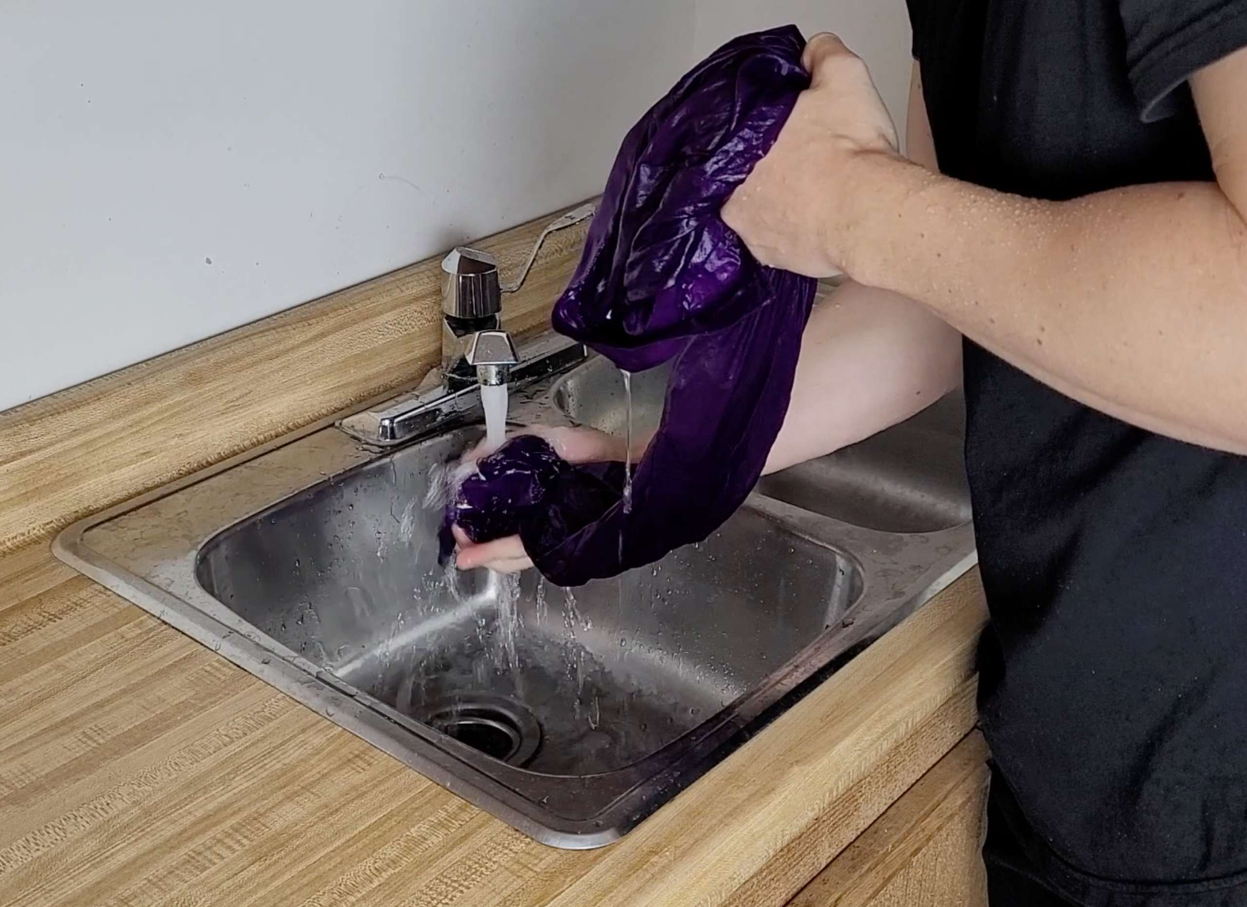 photo of a man rinsing a purple silk shirt under cold water in the sink