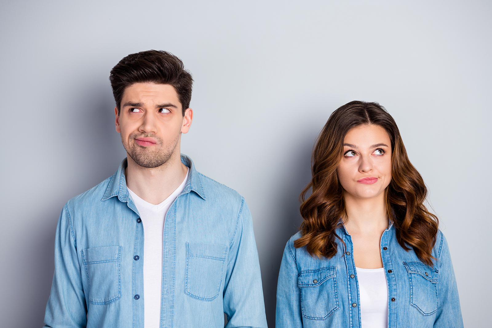 A man and a woman stand side by side against a plain background contemplating a decision looking up to the side.