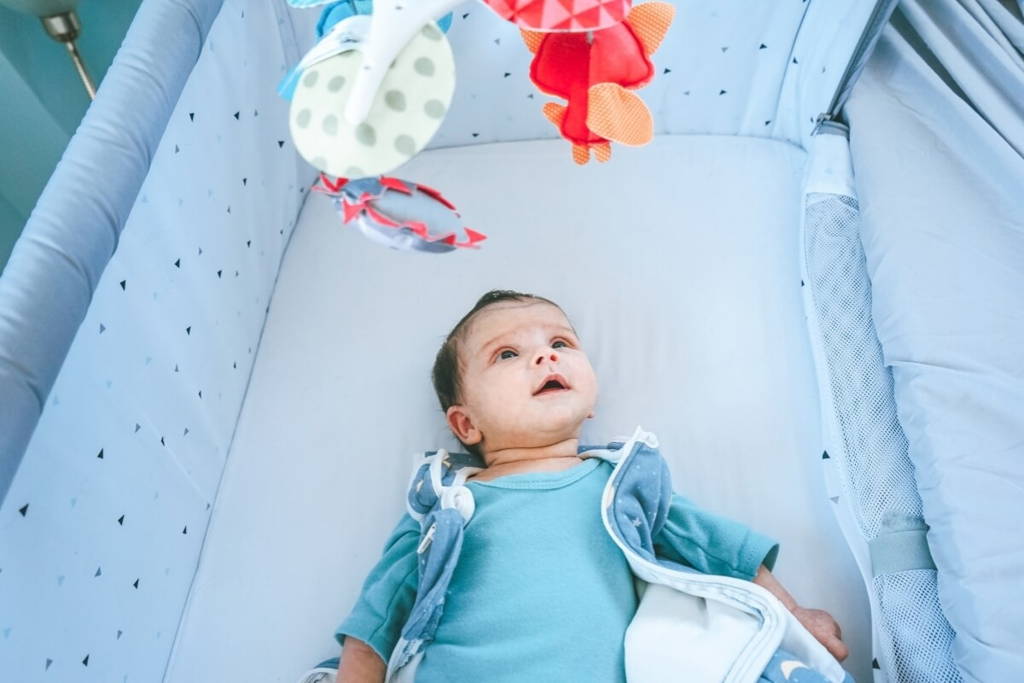Bébé allongé dans son berceau, regardant les jouets mobiles en feutrine suspendus au-dessus de lui.