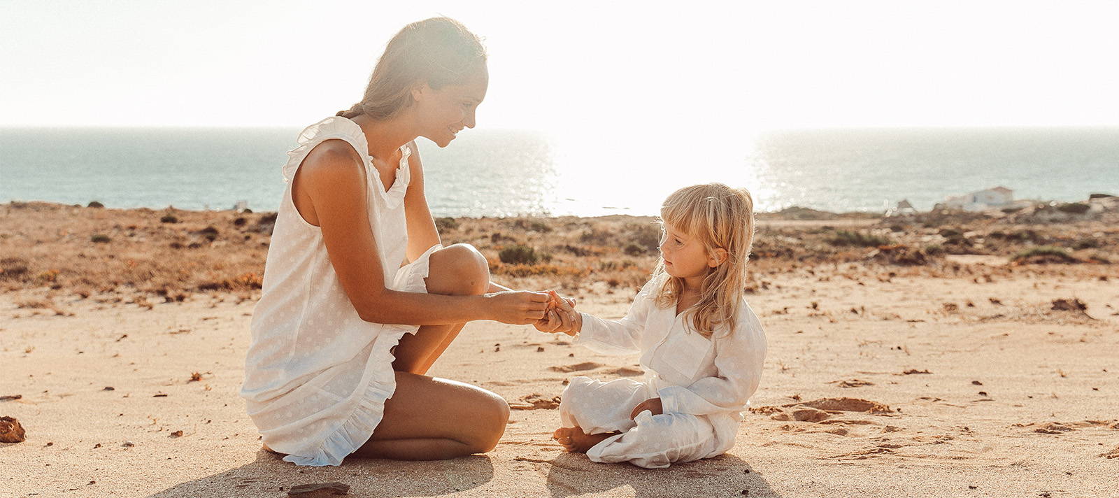 Mother and daughter sharing a secret on the beach matching in  a white cotton nightie and pyjamas 