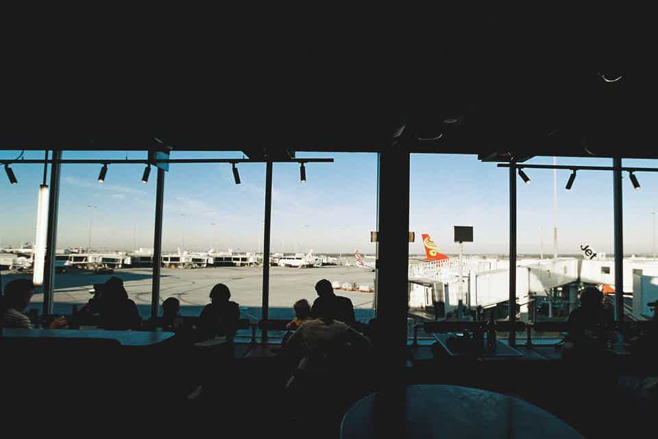 Dark interior of busy cafe with airport scenery of plane runways outside large glass window
