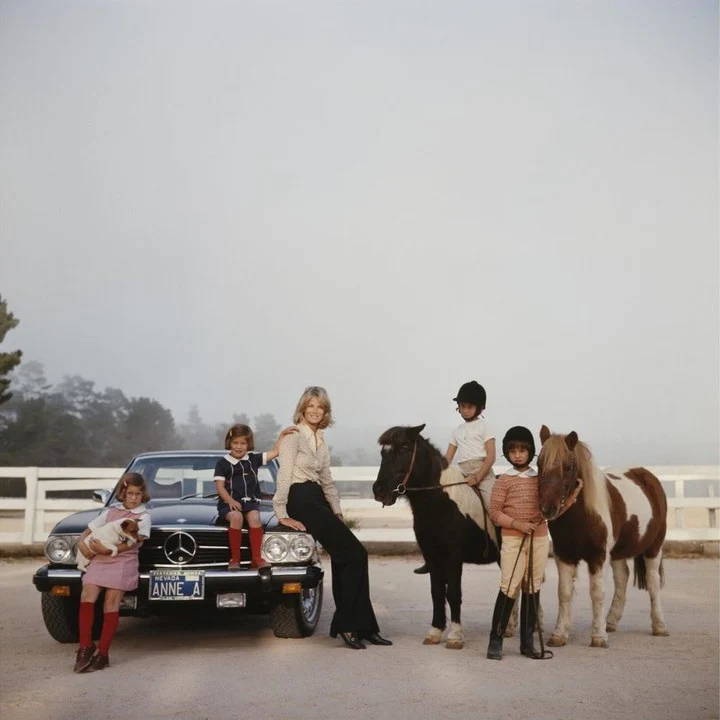 Anne Anka by Slim Aarons – A 1976 photograph of Anne Anka with her daughters and horses, capturing a moment of family life in a luxurious setting.