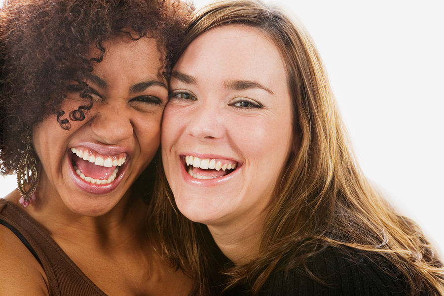 Image of two beautiful women smiling to the camera and close to eachother.
