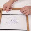 Woman storing her child's doodles and drawings inside a Montessori Keepsake Frame that holds up to 150 papers.