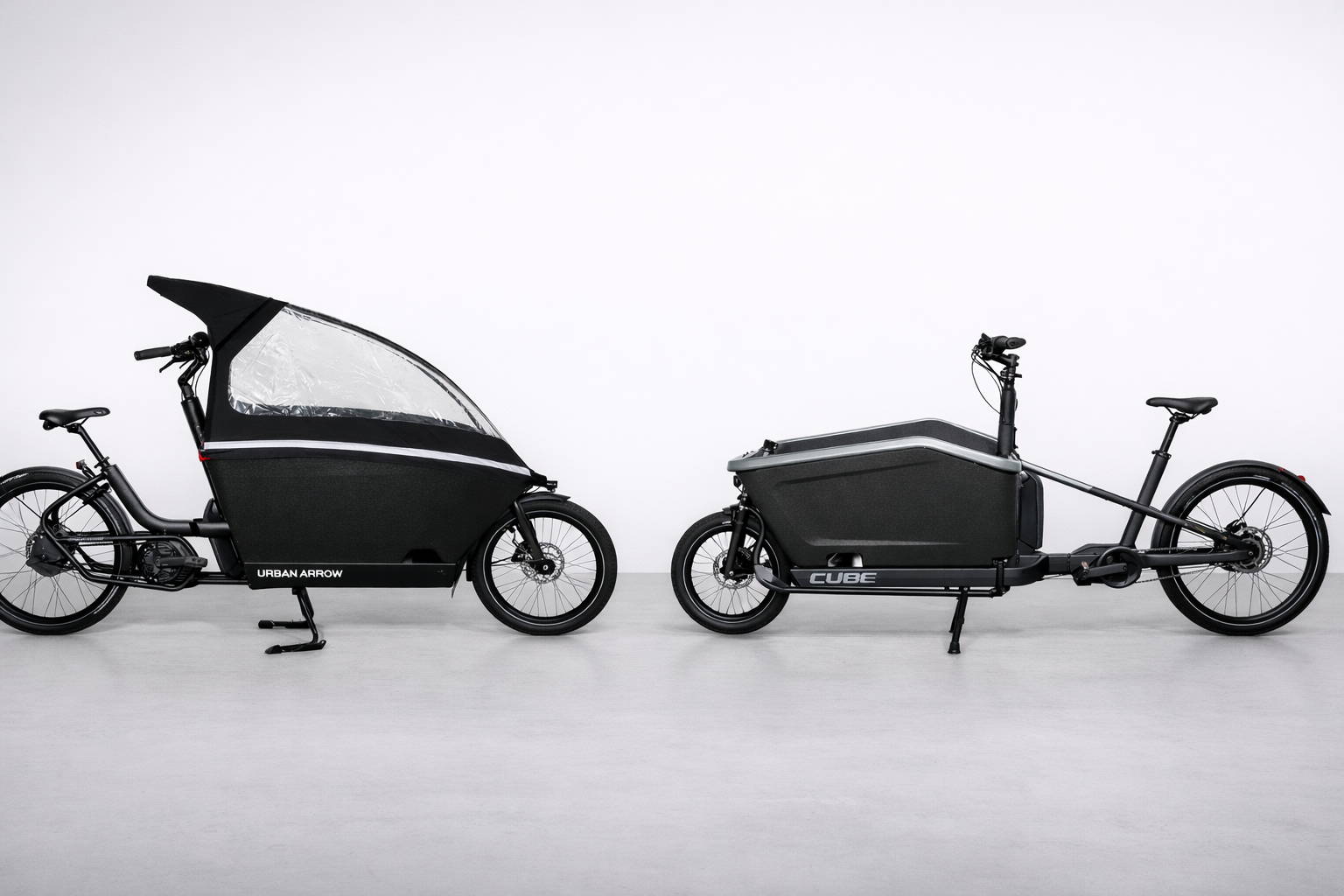 Twee elektrische bakfietsen naast elkaar op neutrale studioachtergrond: links de Urban Arrow Family met gesloten EPP-bak en regenhuif voor kindervervoer, rechts de Cube Cargo Hybrid met open cargobox en lang frame, beide ontworpen voor hoge belasting, dagelijks gebruik en stabiele ondersteuning bij zware lading.