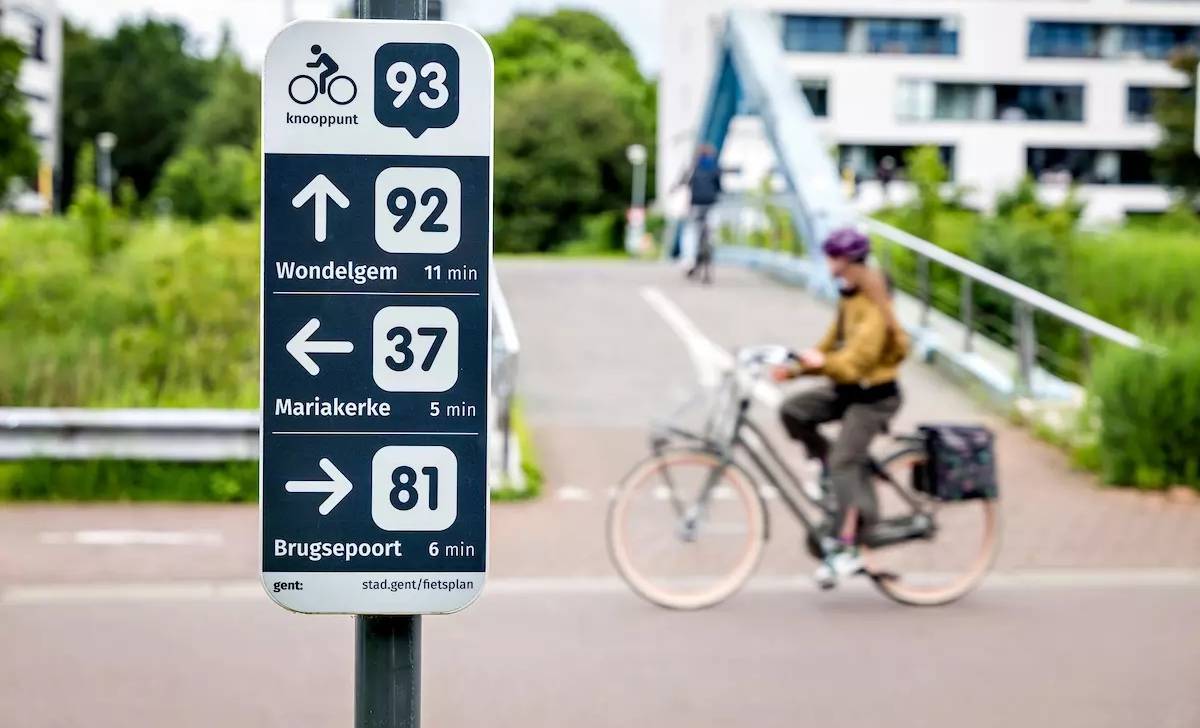 Panneau de points-nœuds cyclables à Gand, avec une cycliste qui passe à l'arrière-plan
