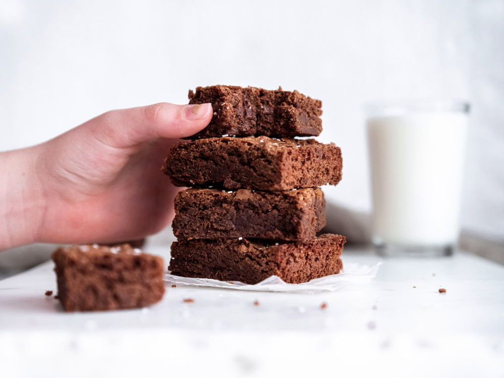 A small hand grabbing the top layer from a stack of delicious brownies